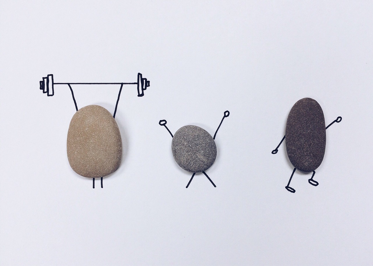 three flat stones lying on a piece of paper with arms and legs drawn around them in black ink. the first is holding up a barbell, the second is doing a jumping jack, and the third is running or doing aerobics